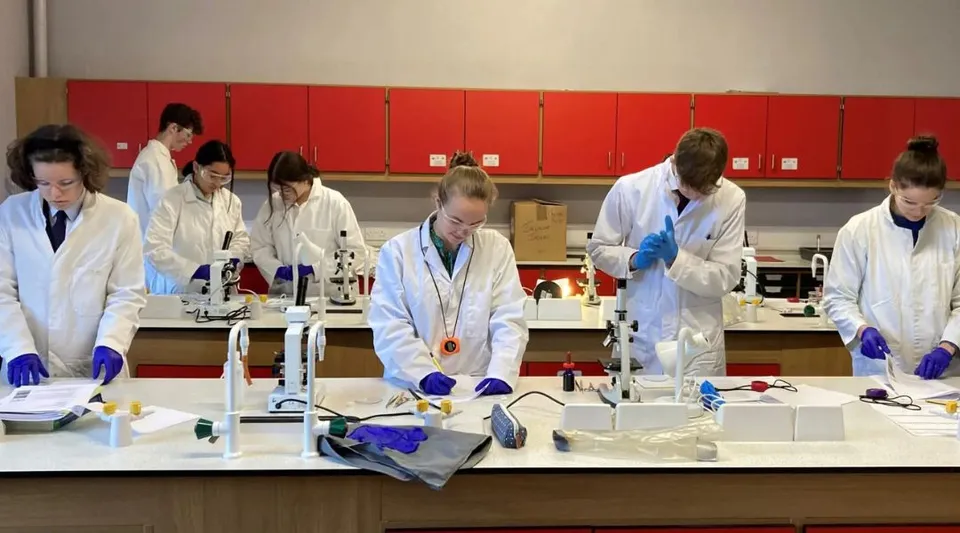 Gli studenti della Longridge Towers School lavorano in camice bianco da laboratorio presso diverse postazioni con attrezzature scientifiche.