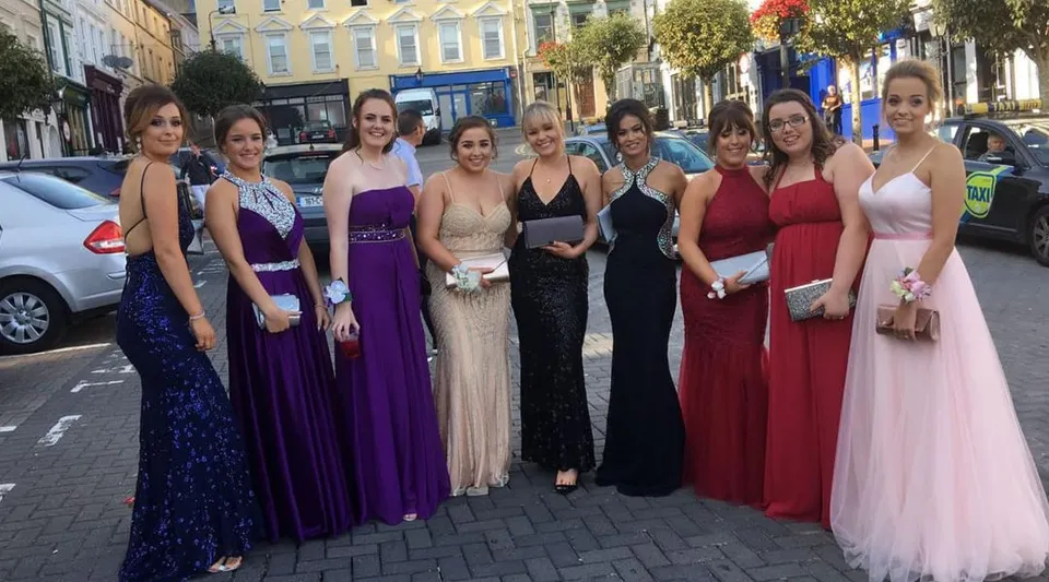 Un gruppo di giovani donne in abiti da festa si trova sulla strada davanti al Carrignafoy Community College.