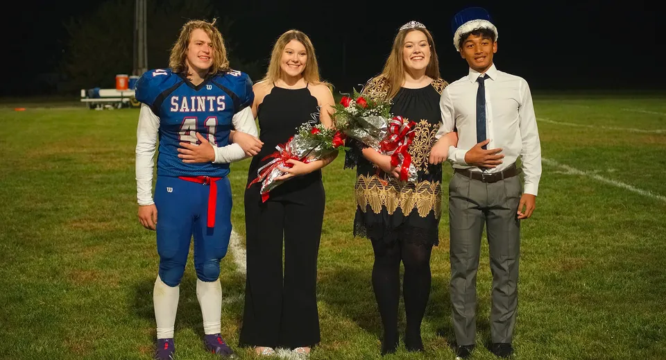 Quattro studenti della Saint Paul Lutheran High School posano con abiti eleganti e divisa da football su un campo sportivo.