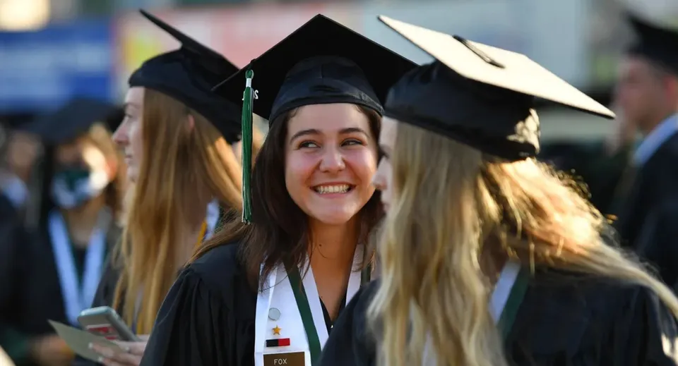 Una neodiplomata sorridente in toga sta insieme ad altri diplomati nel campus della Harbour View High School.