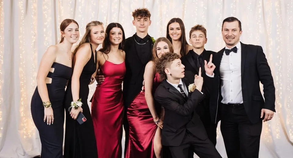 Un gruppo di persone in abbigliamento formale in posa davanti a un sipario nel campus del Pakuranga College.