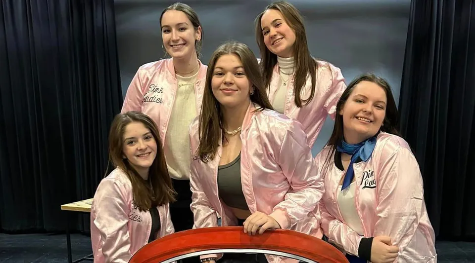 Un gruppo di giovani donne in outfit rosa coordinati è in piedi davanti a uno sfondo scuro nel campus della Haliburton Highlands School.