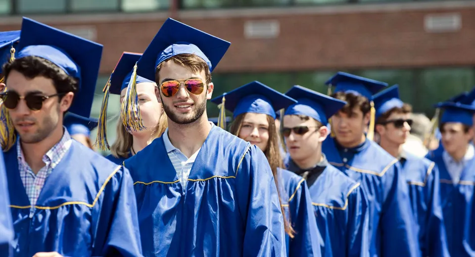 Un gruppo di diplomati della Osgoode Township High School sta davanti a un edificio in mattoni con toghe e tocchi blu.