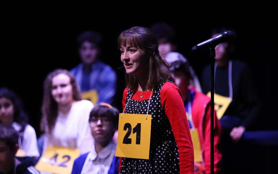 Una studentessa della Lake Ridge Academy parla davanti a un microfono su un palco con un cartellino numerato al collo.