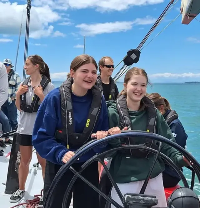 Dos chicas al timón de un velero con chaleco salvavidas en mar abierto