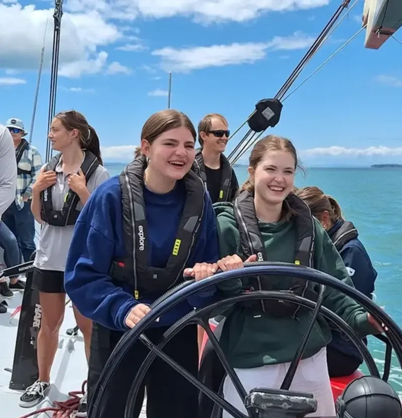 Dos chicas al timón de un velero con chaleco salvavidas en mar abierto