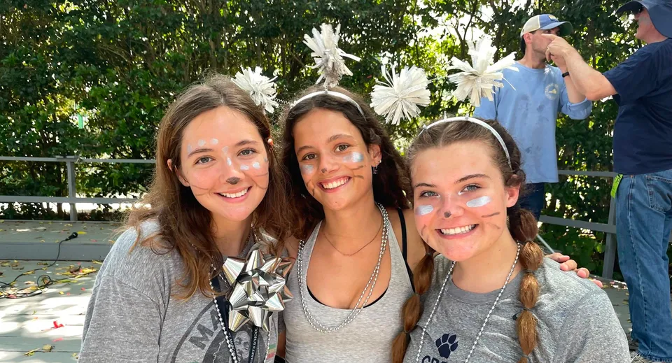 Tre studentesse della St. Margaret's School posano all'aperto davanti ad alberi e cespugli verdi.