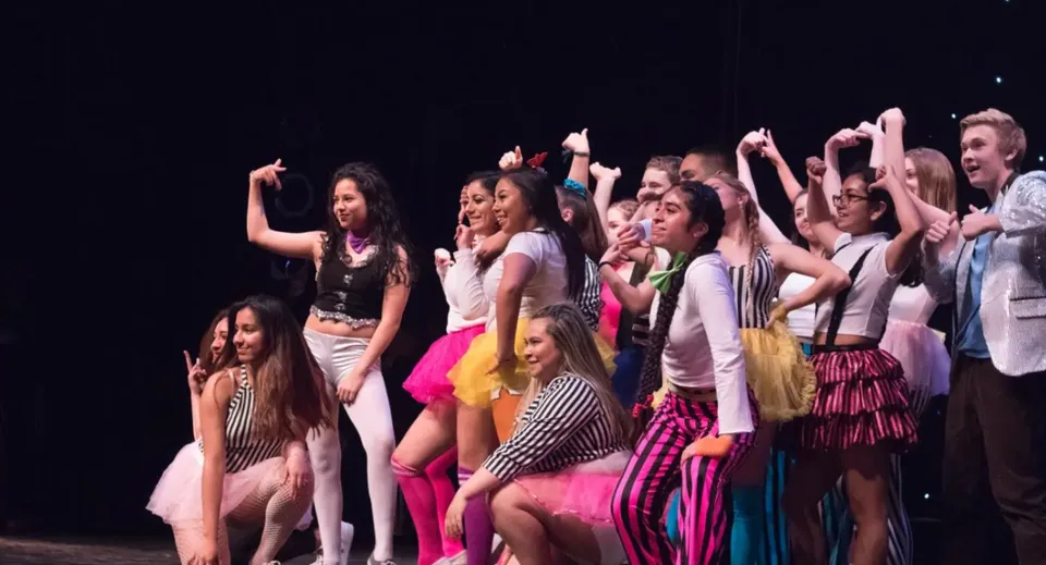 Un gruppo di giovani studentesse del Ballybay Community College si esibisce su un palco con uno sfondo scuro.