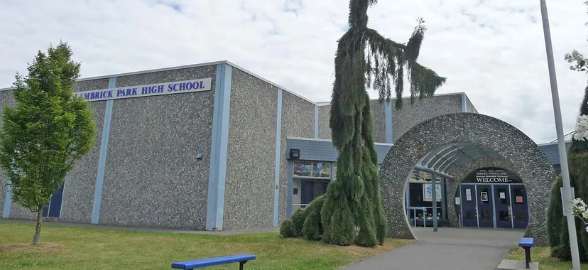 L'edificio moderno della Lambrick Park Secondary School con un sottile cipresso in primo piano davanti a un cielo nuvoloso.