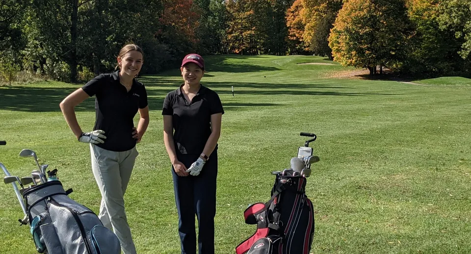 Due persone in abbigliamento da golf si trovano sul campo da golf ben curato vicino alla Sir Robert Borden High School in un ambiente autunnale.
