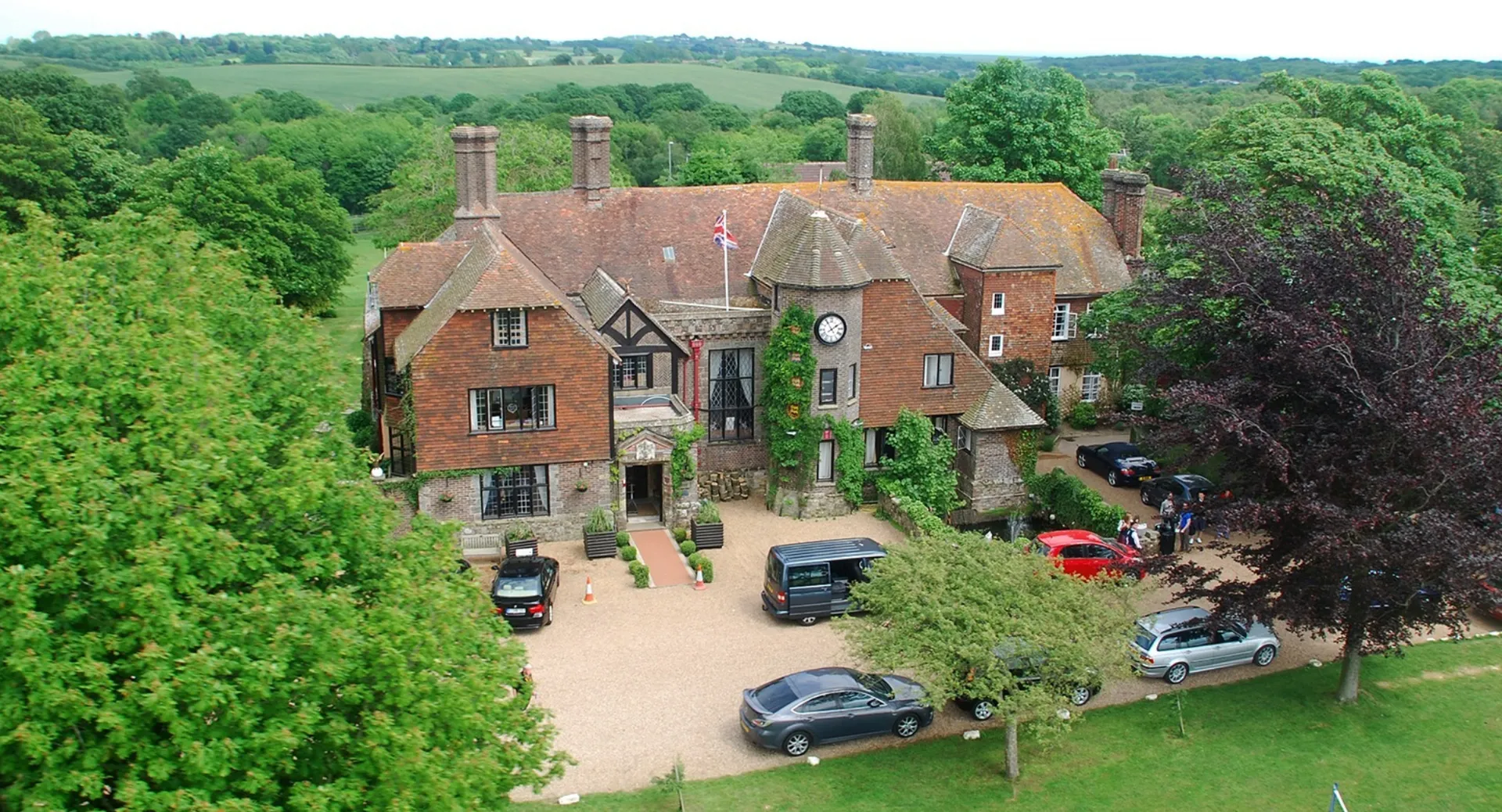 Una villa in stile Tudor circondata da un verde paesaggio nel campus della Buckswood School, con auto parcheggiate in primo piano.