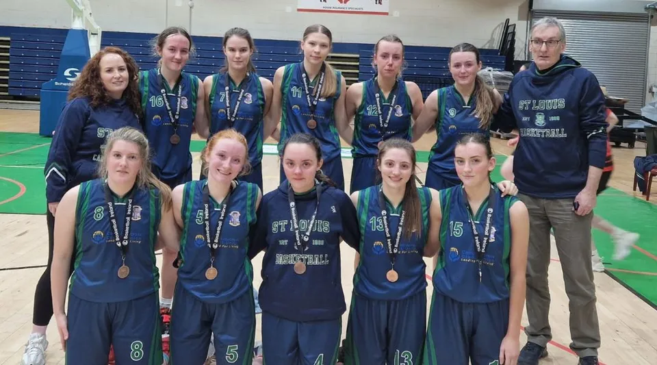 Un gruppo di giovani atlete in divisa sportiva posa davanti a un campo da basket nel campus della St. Louis Secondary School.
