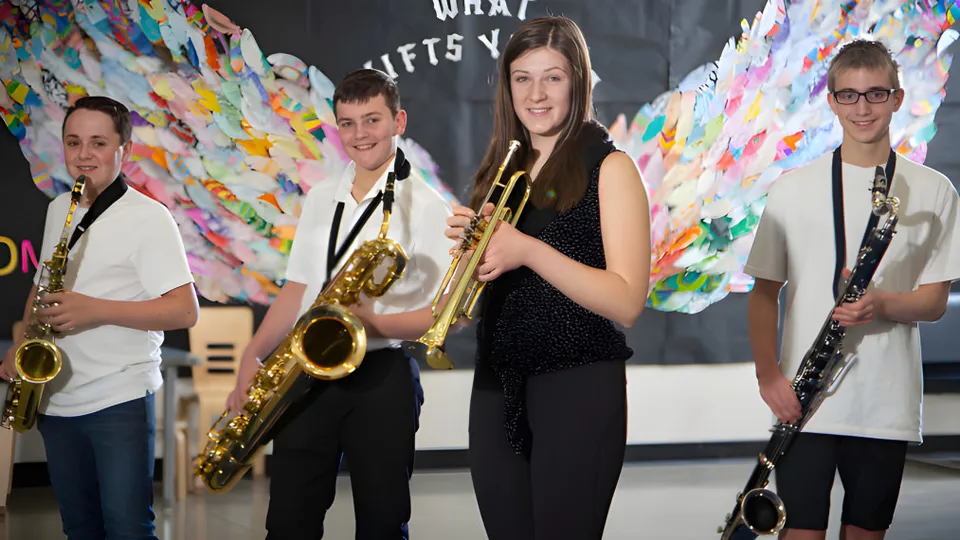 Un gruppo di musicisti si trova davanti a uno sfondo astratto e colorato nel campus della École Dansereau Meadows School.