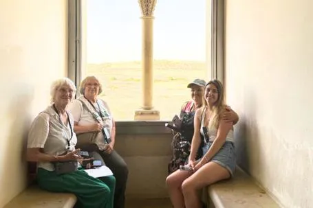 Cuatro mujeres posan sentadas junto a un gran ventanal con columnas y vistas al exterior