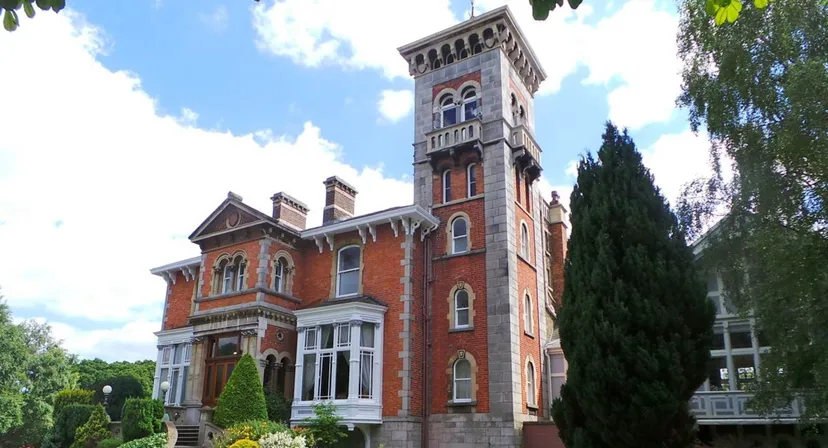 L'imponente edificio in mattoni con un'alta torre nel campus del St. Michael's College si trova circondato da una verde vegetazione sotto un cielo azzurro.