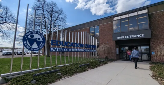 Das Backsteingebäude mit dem Eingang und dem Logo des Waterloo Region District School Board ist von Bäumen und einem gepflasterten Weg umgeben.