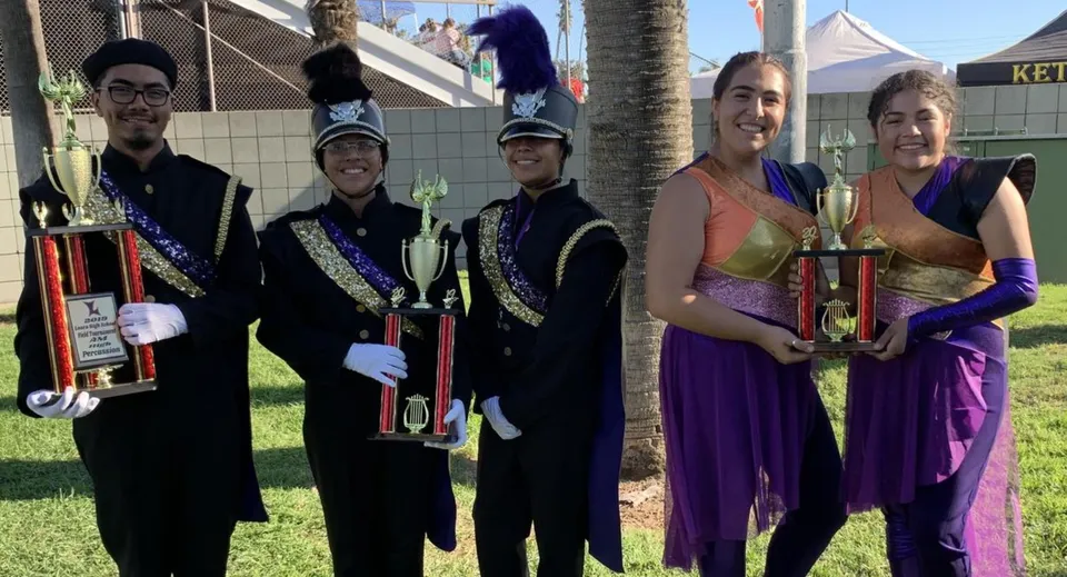 Studenti della Bell High School in costumi colorati tengono i loro trofei davanti a un festival con tende e palme.