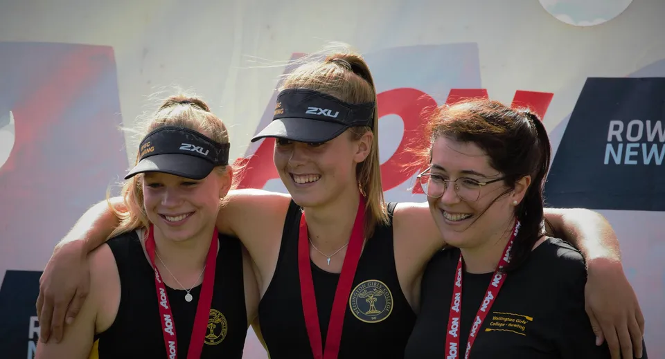 Tre studentesse del Wellington Girls' College posano insieme davanti a uno sfondo colorato.
