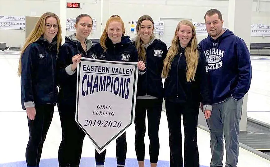 Estudiantes de la G.W. Graham Secondary School sostienen una pancarta como Eastern Valley Champions en Girls Curling 2019/2020.