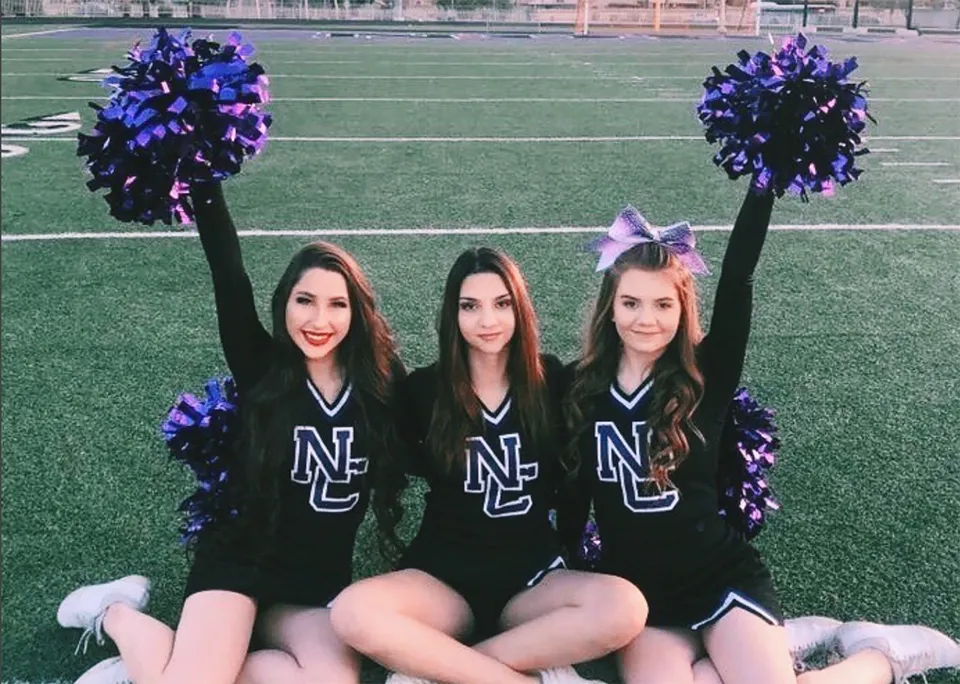 Tre cheerleader della North Canyon High School si trovano su un campo verde e tengono in mano pompon viola e neri.