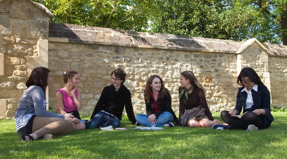 Un gruppo di studentesse è seduto sul prato davanti a un muro di pietra nel campus del Greene's College Oxford.