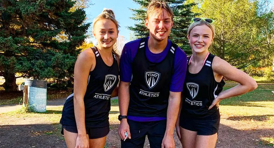 Tre studenti della Vimy Ridge Academy sono insieme all'aperto in divise sportive di squadra davanti a uno sfondo simile a un parco.