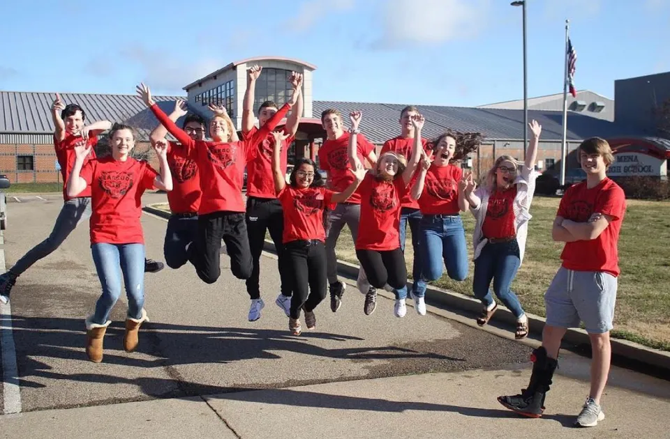 Un gruppo di giovani con magliette rosse salta in aria davanti all'edificio della Mena High School.