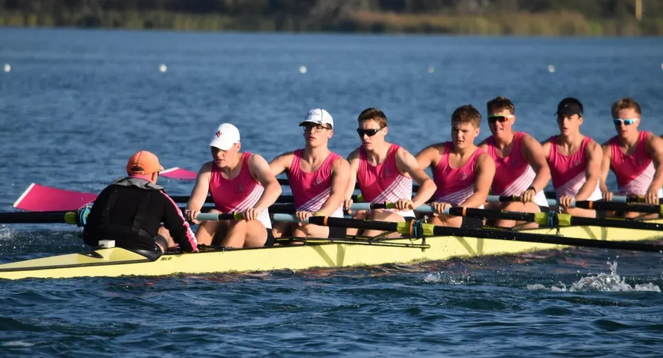 Un gruppo di studenti della Christ's Hospital School rema in divise rosse su una barca gialla in un lago calmo.