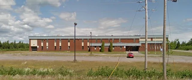 El edificio de ladrillo de varios pisos de Botwood Collegiate con un coche rojo en primer plano está rodeado por un césped.