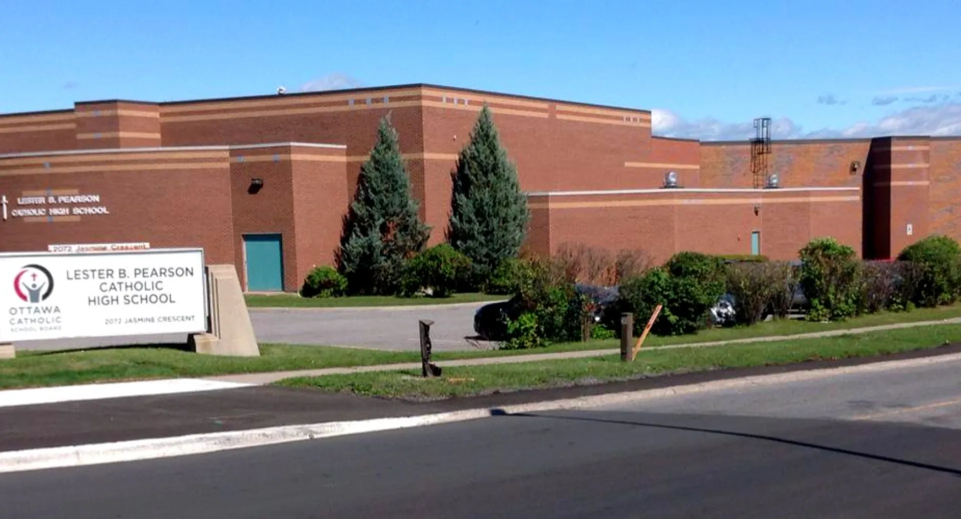 L'ampio edificio in mattoni della Lester B. Pearson Catholic High School con un cartello davanti agli alberi e un parcheggio sullo sfondo.
