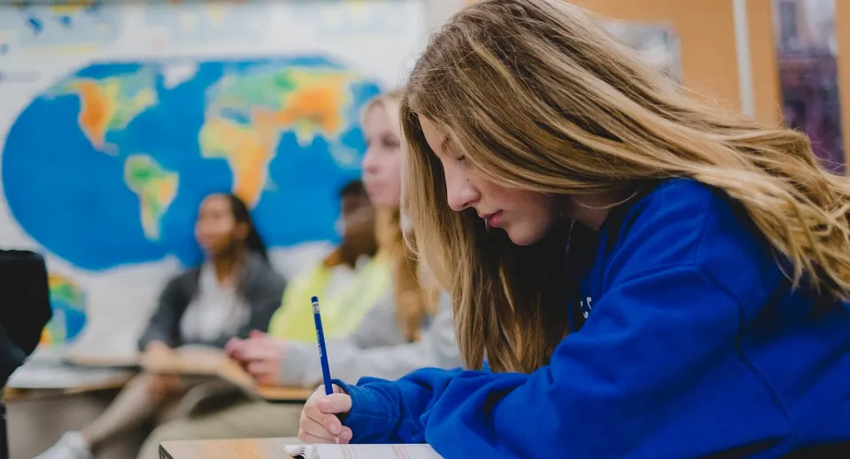 Una studentessa della Christian Life School lavora concentrata davanti a una mappa del mondo a colori.