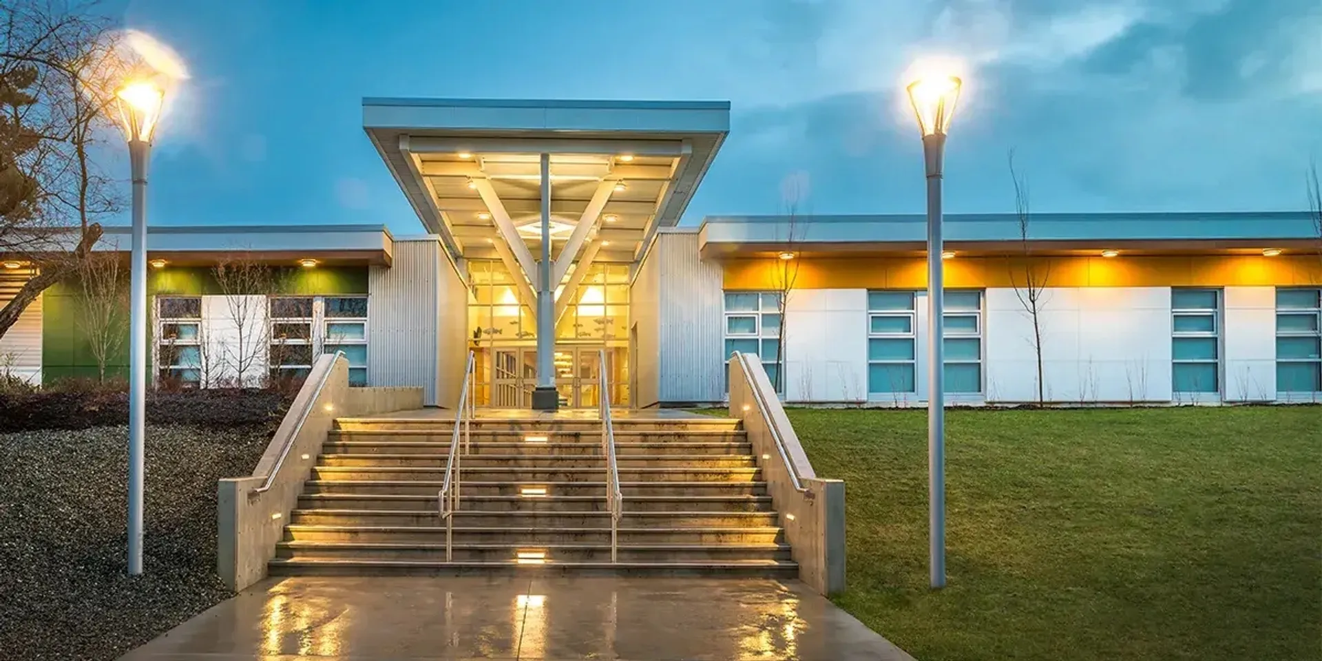 L'ingresso illuminato della Georges Vanier Secondary School con un'ampia scalinata e due lampioni al crepuscolo.