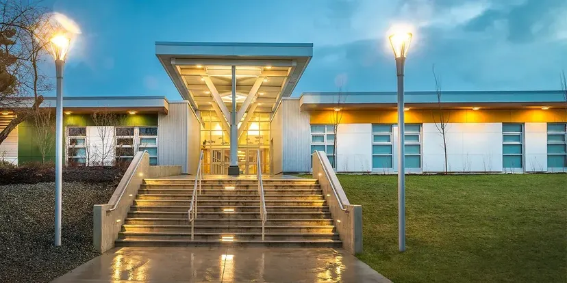 L'ingresso illuminato della Georges Vanier Secondary School con un'ampia scalinata e due lampioni al crepuscolo.