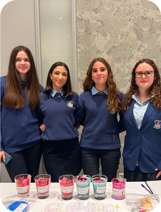 Cuatro estudiantes con uniforme escolar posan tras una mesa con velas artesanales