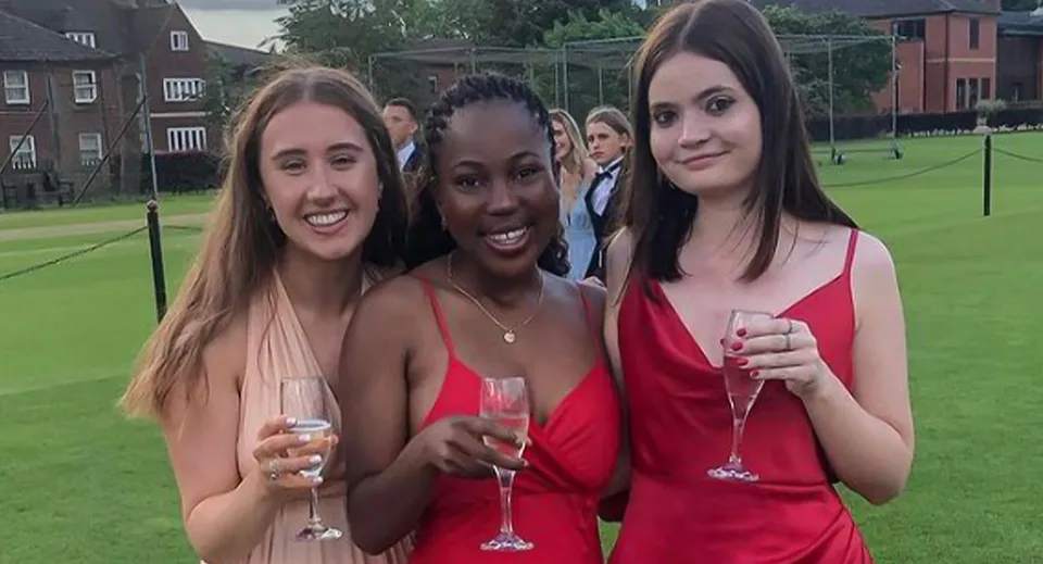 Tre studentesse della Oakham School sono su un prato e tengono dei calici da spumante.
