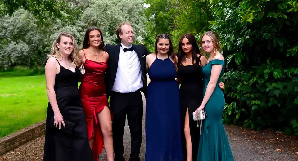 Un gruppo di persone vestite in modo elegante posa nel verde del campus della Taunton School International.