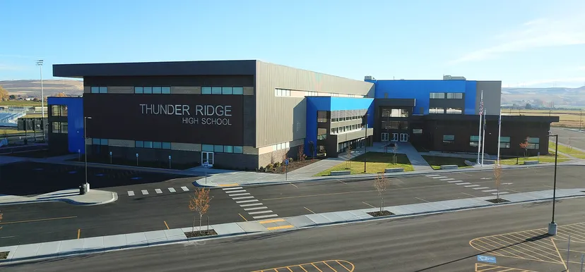 Il moderno edificio a più piani della Thunder Ridge High School si stagli contro un cielo azzurro terso, con un'area pavimentata e strisce pedonali.