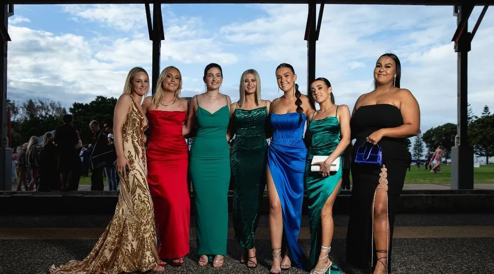 Sei studentesse della Warners Bay High School si trovano in abito da sera davanti a uno sfondo paesaggistico con il cielo nuvoloso.
