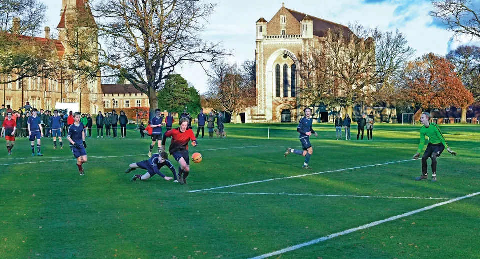 Un gruppo di studenti gioca a rugby sul campo della Charterhouse School davanti a un edificio storico.