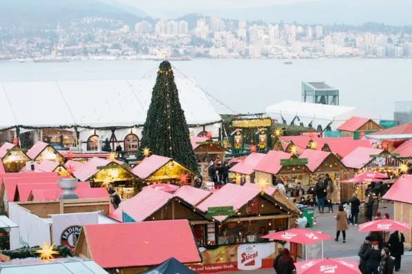 Mercado navideño al aire libre con casetas de tejado rojo y un gran árbol decorado