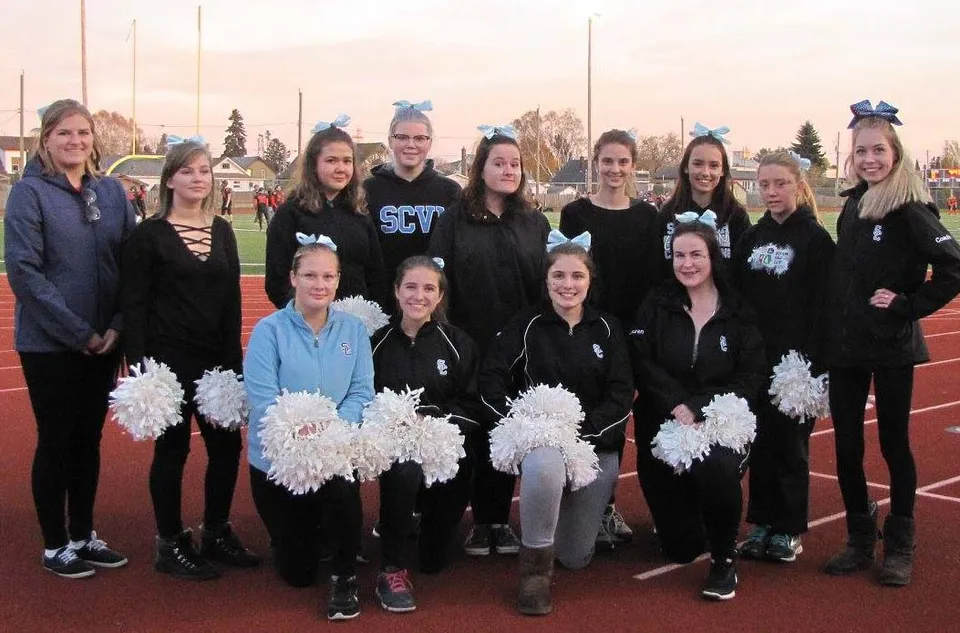 Un gruppo di cheerleader in divisa nera e con pompon bianchi sta sul campo sportivo del Superior Collegiate & Vocational Institute.