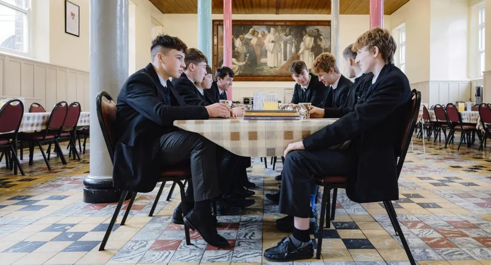 Un gruppo di studenti del Cistercian College in abito formale è seduto attorno a un tavolo in un ambiente accademico.
