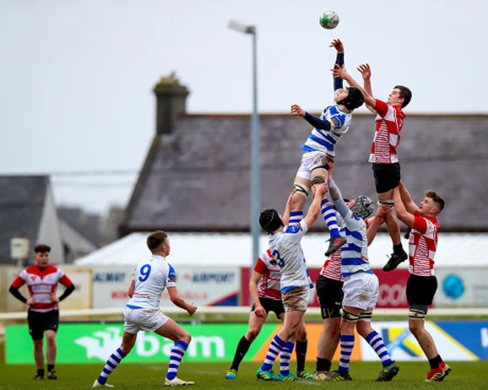 Due giocatori di rugby si contendono la palla in aria davanti a un edificio storico nel campus del C.B.S. Roscommon.