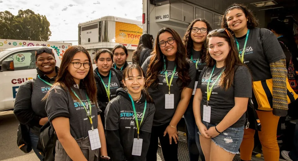 Un gruppo di studentesse della Tree of Life Christian School con magliette verdi e nere sta all'aperto davanti a dei veicoli.