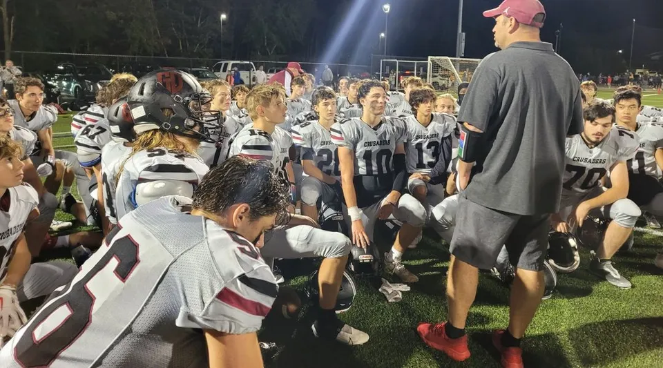 Un gruppo di giovani calciatori del Groton-Dunstable Regional School District si riunisce di notte sul campo di gioco con un allenatore.