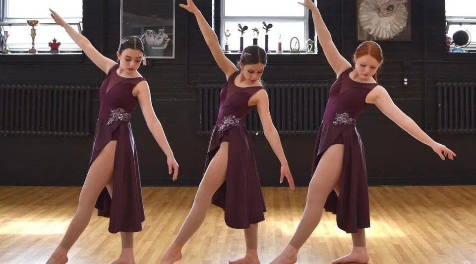 Tre studentesse con abiti color bordeaux della Macdonald High School eseguono una coreografia di danza in uno studio.