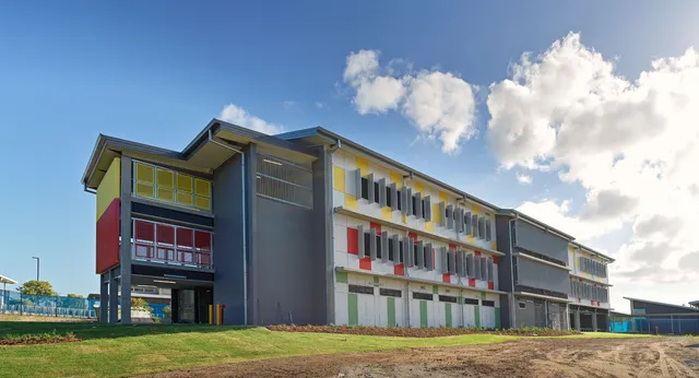 L'edificio a più piani del Burpengary State Secondary College mostra una facciata colorata contro un cielo blu e un prato verde.