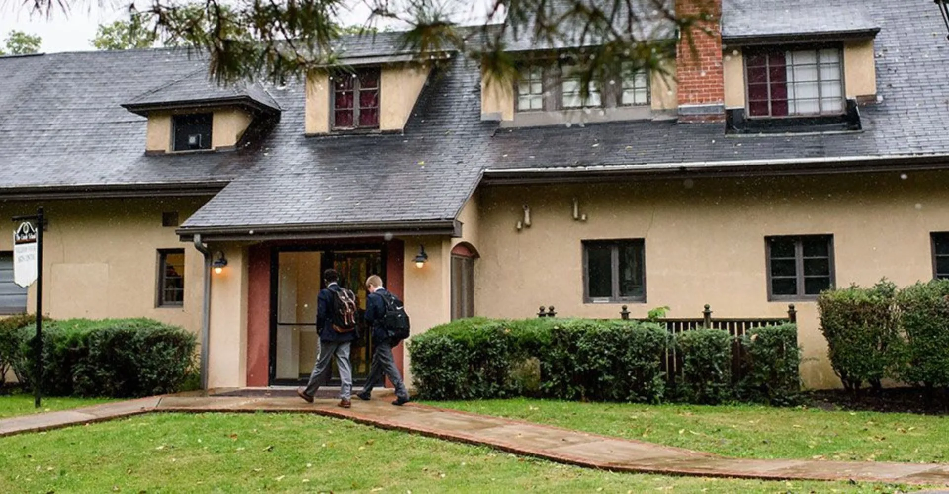 L'edificio in mattoni a due piani con veranda nel campus della The Linsly School con due persone all'ingresso.