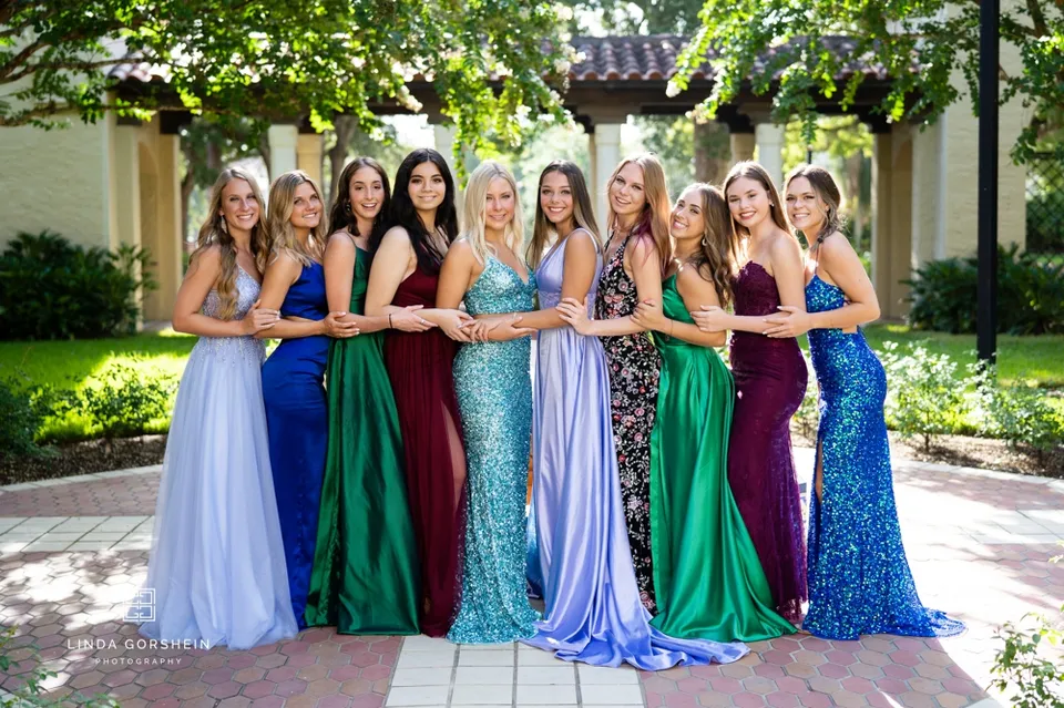 Un gruppo di studentesse della Lake Mary Preparatory School insieme, con abiti colorati, in un giardino con alberi e architettura.