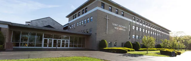 L'edificio in mattoni della Saint Anthony's High School con una croce sulla facciata e un viale d'ingresso decorato con piante.